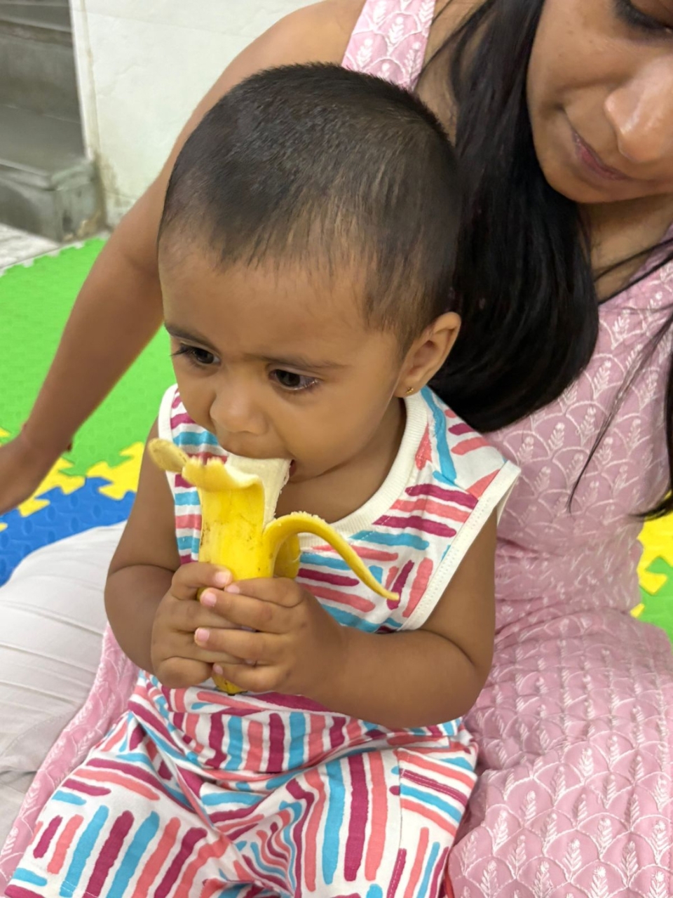 Baby eating a banana while sitting on a lap