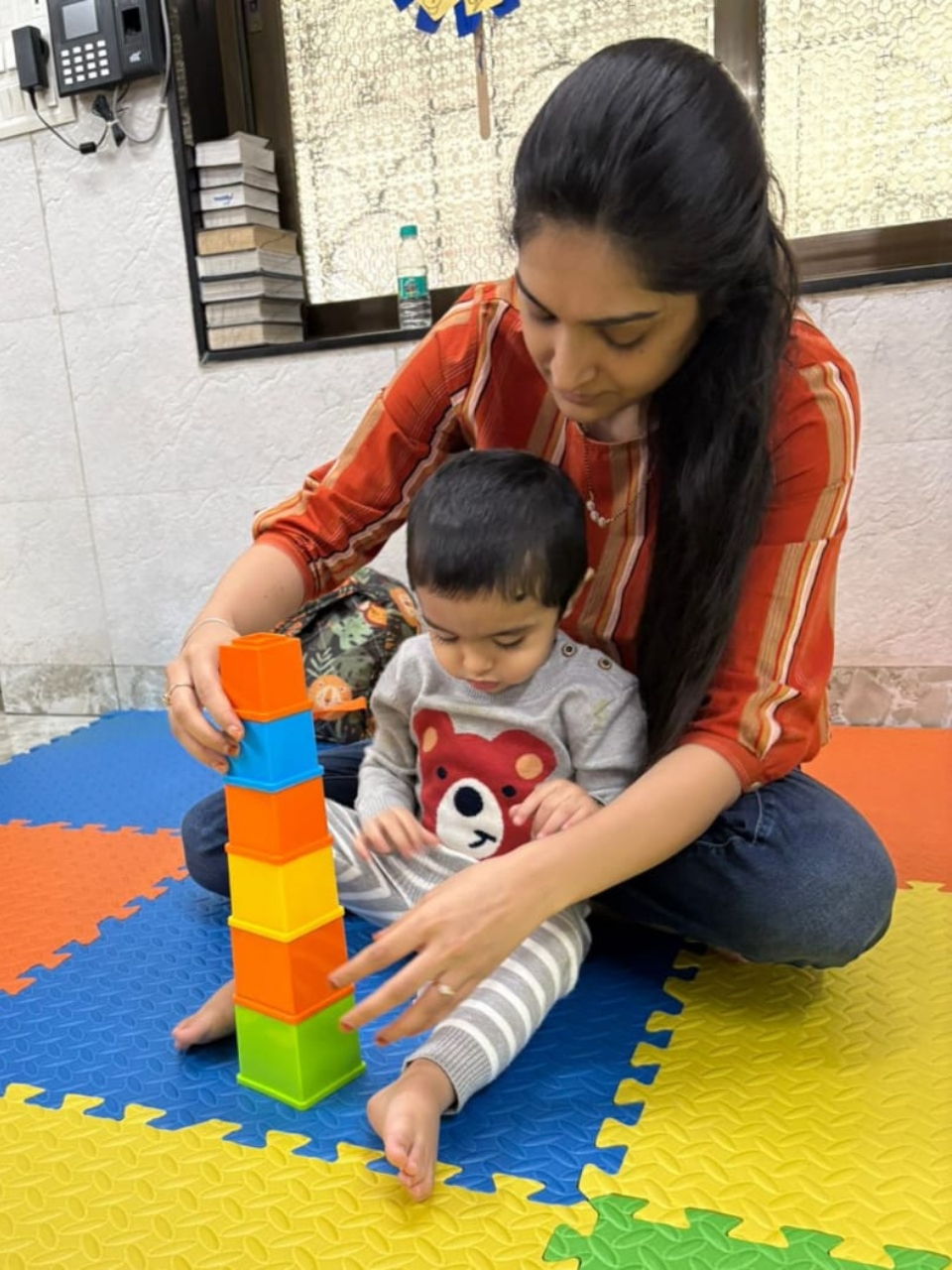 Toddler stacking colorful blocks with guidance from a woman.