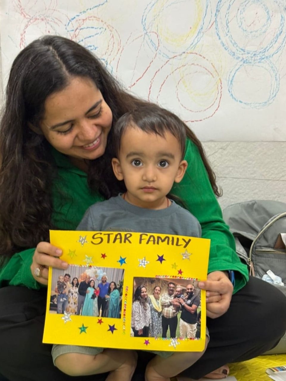 Child holding a yellow “Star Family” craft while sitting on a teacher’s lap, both smiling.